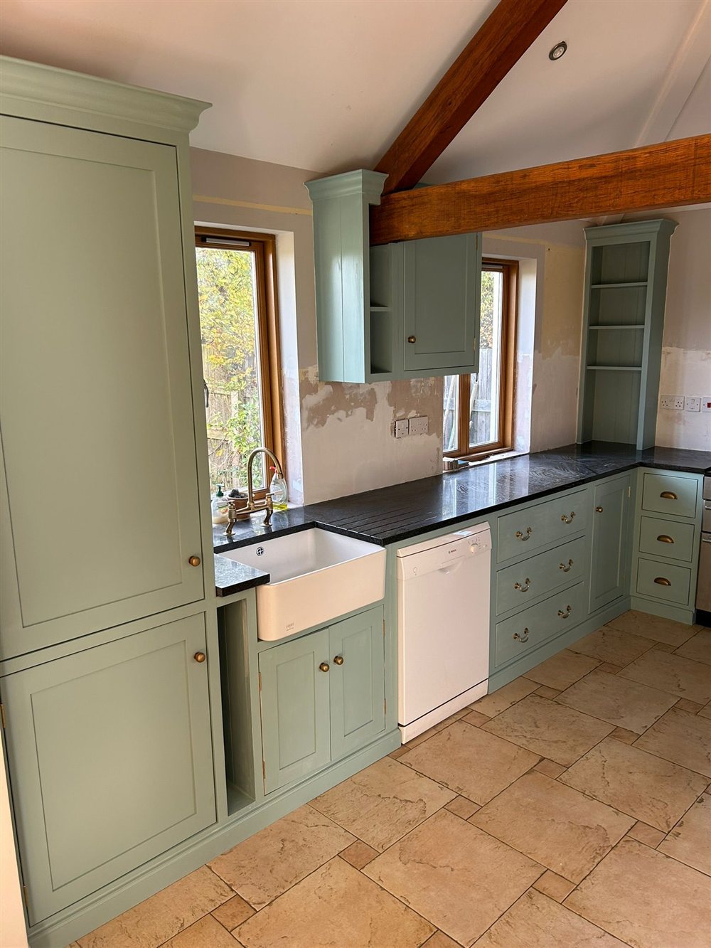 Painted kitchen cabinetry beside a Belfast sink, with an exposed oak beam following the roofline.