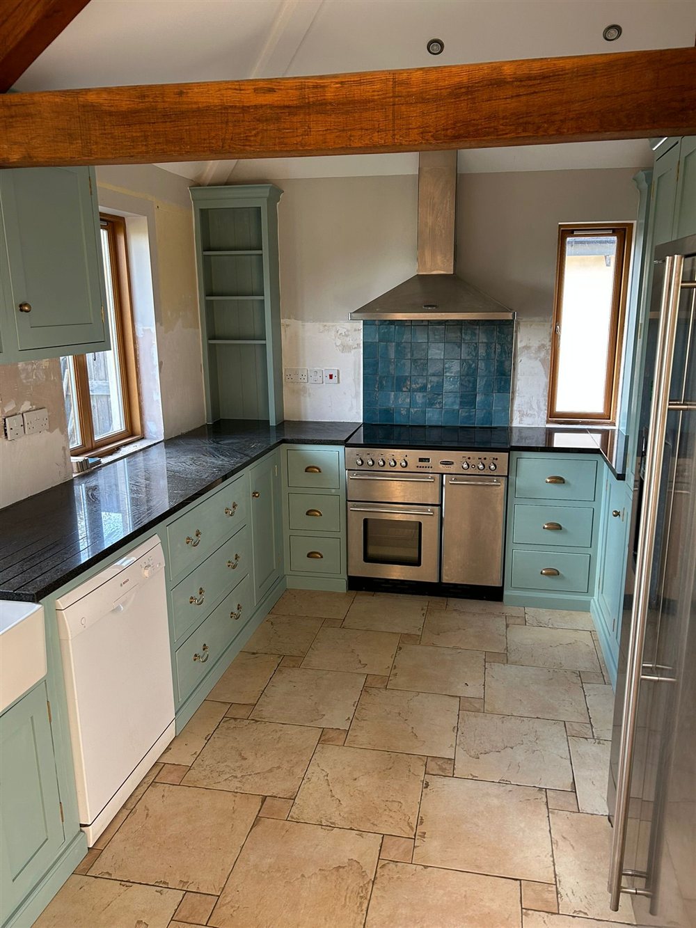 Painted kitchen cabinetry around a range cooker and tiled splashback, with an exposed oak beam crossing the ceiling.